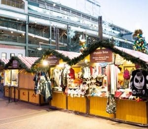 Outdoor Christmas market stalls decorated with garlands, selling clothing and accessories, including a panda-themed bag.