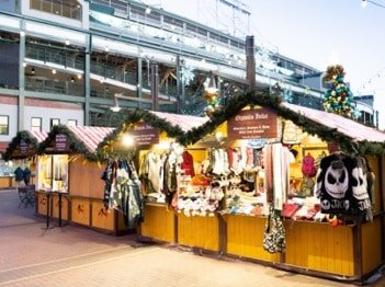 Outdoor Christmas market stalls decorated with garlands, selling clothing and accessories, including a panda-themed bag.